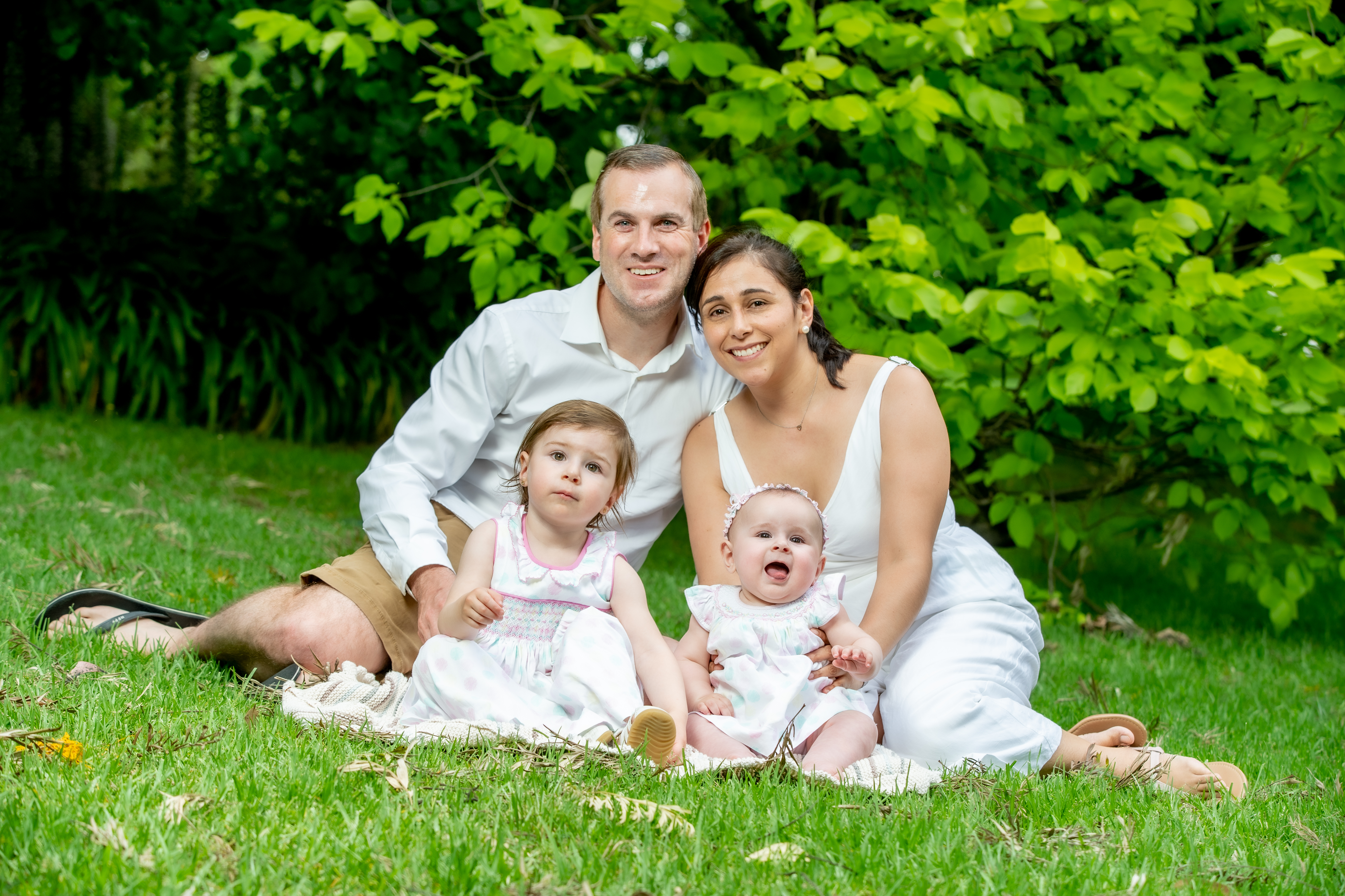 A family sitting on the grass. Mother, father and 2 young daughters.